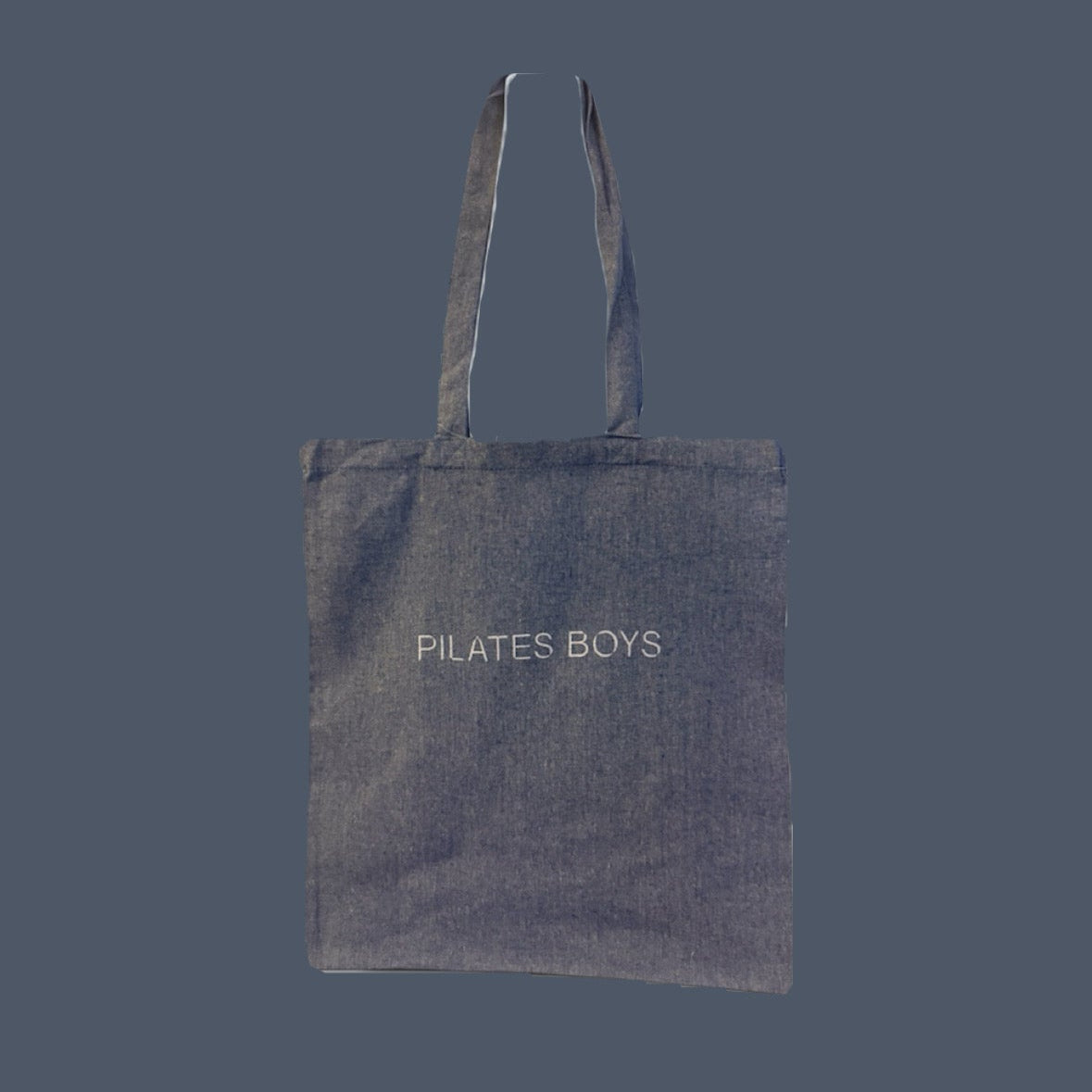 A dark blue canvas tote bag with 'PILATES BOYS' printed in white text on the front, set against a solid dark gray background.